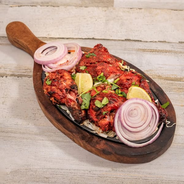 Deccan Flavors' Indian chicken tikka, garnished with lime and red onion, served on a wooden platter.