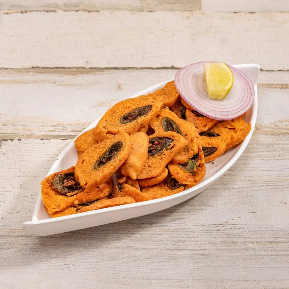 Deccan Flavors' Indian snack, a white boat-shaped dish filled with fried, spiced rolls, garnished with onion and lemon.