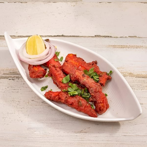 Red Indian chicken appetizer, garnished with cilantro, onion, and a lemon wedge on a white plate.